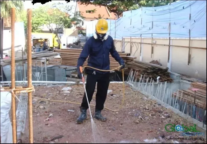 Kỹ thuật viên phun thuốc phòng mối lên nền đất hố móng giữa các cây thép chờ